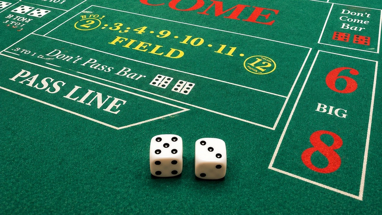 Two dice resting on the green felt of a craps table, beside the Pass Line and Field betting areas.